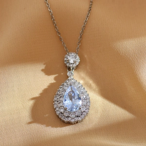 Macro detail of teardrop light blue gemstone pendant with double diamond halo on silver chain