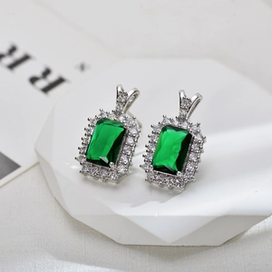 Close-up of emerald-cut green zircon earrings with shimmering halo in silver setting