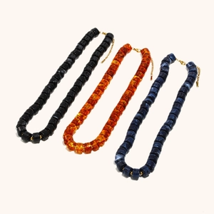 Detailed view of layered 18K gold plated acrylic beaded necklaces in amber, black, and marble