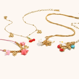 Detail of 18K gold-plated beaded bracelet with red cherry and star charms on beige background