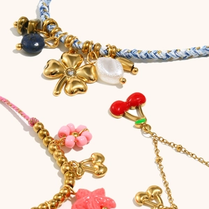 Macro detail of bohemian braided rope bracelets with 18K gold plated cherry and clover charms