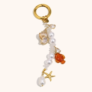 Golden sea shell and starfish keychain with white pearls and orange fish charm on beige base