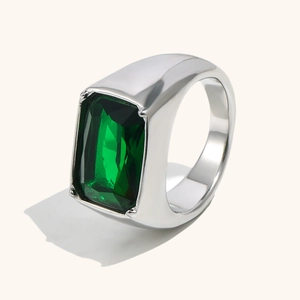 Modern emerald cut green stone signet ring in polished silver finish on beige background