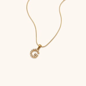 Dettaglio di una collana a catena serpente dorata con ciondolo a lettera G e perle