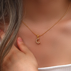 Dettaglio di una collana a catena serpente dorata con ciondolo a lettera C e perle