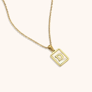 Détail d'un collier doré avec pendentif carré en nacre blanche et lettrage D gravé