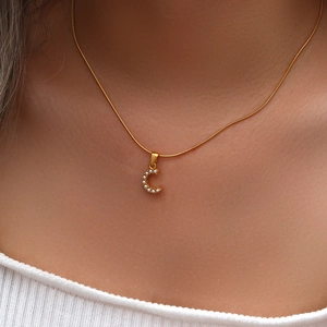 Dettaglio macro di una collana a catena serpente dorata con ciondolo lettera C e perle