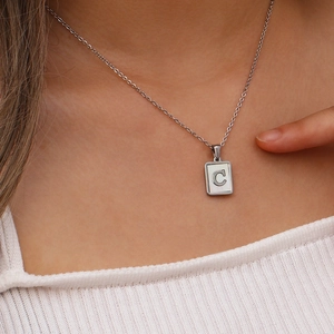 Gros plan d'un pendentif carré en acier argenté avec lettre C en nacre blanche