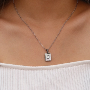 Détail macro du collier carré argenté avec nacre et lettre C porté par un mannequin