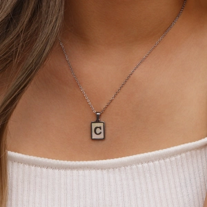 Gros plan d'un collier argenté avec pendentif en nacre et lettre C métallique