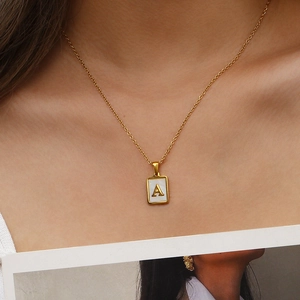 Gros plan du pendentif rectangulaire doré avec lettre A et nacre sur le cou d'une femme