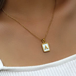 Détail d'un collier avec pendentif carré doré en nacre blanche et la lettre A gravée