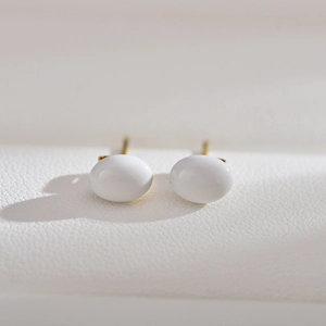 Macro shot of minimalist white oval pearl studs with golden posts on leather texture