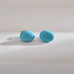 Detail of bright blue oval turquoise-style stud earrings with gold-tone metal posts