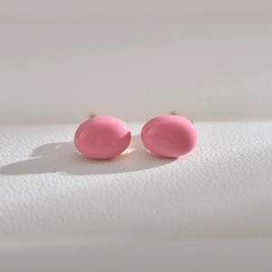Close-up of pink oval freshwater pearl earrings with gold-toned metal posts on white leather