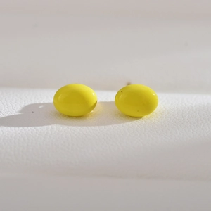 Macro shot of oval bright yellow pearl earrings on white textured leather background