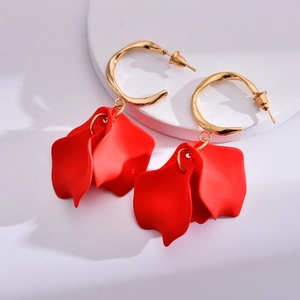 Macro detail of gold C-ring earrings with matte red acrylic flower petals on a white base