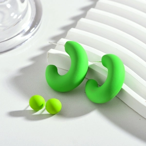 Gros plan de boucles d'oreilles en C et clous vert néon mat sur présentoir blanc
