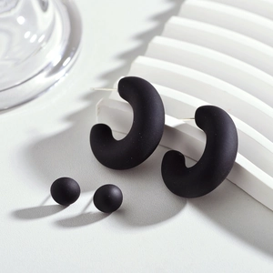 Détail de boucles d'oreilles en acrylique noir mat en forme de C et clous assortis épurés