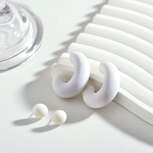 Détail de boucles d'oreilles créoles C en acrylique blanc mat et clous sur support