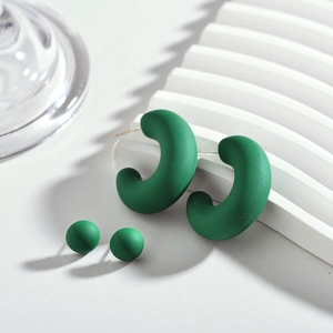 Détail de boucles d'oreilles en acrylique vert mat en forme de C et boule sur socle blanc