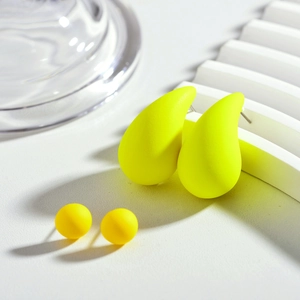 Détail de boucles d'oreilles goutte jaune néon et puces mates sur socle blanc rayé