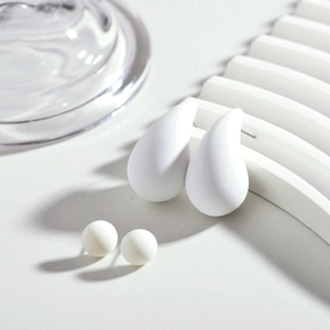 Vue macro de boucles d'oreilles goutte blanches mates et de puces sur décor épuré