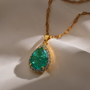 Detailopname van druppelvormige smaragd hanger met zirkonia halo aan gouden ketting