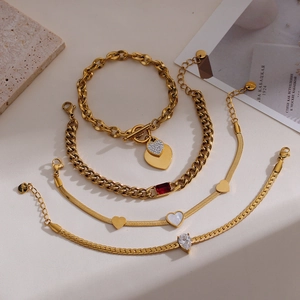 Golden stainless steel bracelet set with heart charms and red gemstone on marble background