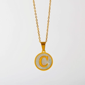 Detail van gouden ketting met ronde witte schelphanger en gegraveerde letter C