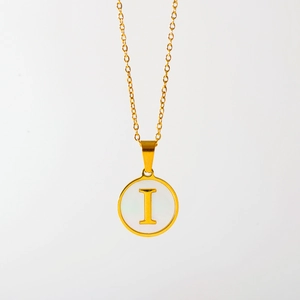 Macro detail van gouden letter I hanger met witte schelpinleg op een fijne ketting
