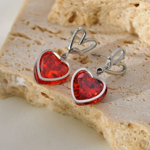 Dettaglio macro di orecchini a cuore in argento con cristalli rossi su sfondo di pietra