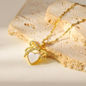 Détail du pendentif cœur doré avec nœud en perles et incrustation en nacre blanche