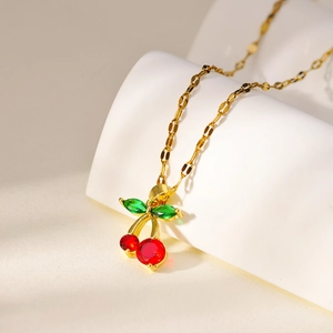 Macro view of cherry-shaped gold necklace featuring red and green crystal pendants