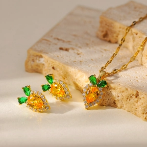 Cute carrot jewelry set with orange gemstones and green leaves on beige stone