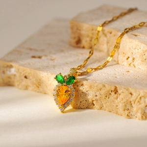Cute carrot pendant necklace with orange and green gems on a textured stone