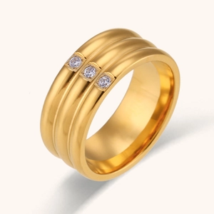Vue détaillée d'une large bague en acier doré sertie de trois zircons cubiques clairs