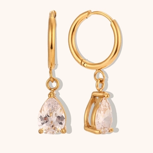 Détail de créoles dorées avec pendentif en zircone poire sur un fond épuré blanc