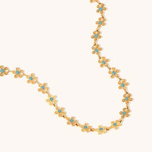 Detail of gold floral necklace with light blue daisy beads on a neutral background