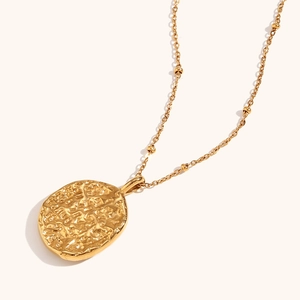 Macro shot of gold hammered oval pendant with textured finish on beaded chain necklace