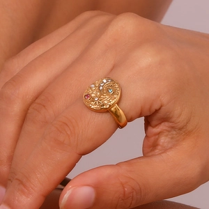 Detail of gold oval ring with embossed moon, star and eye icons and colored crystals