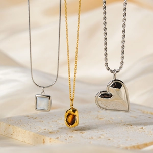 Three elegant gold and silver necklaces featuring heart and stone pendants on a stone background