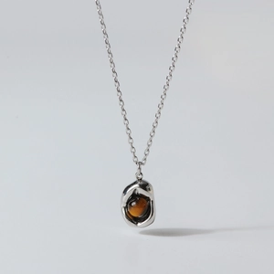 Macro shot of silver-tone irregular heart pendant with a round brown tiger eye gemstone