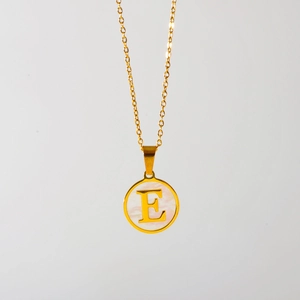Detail van de gouden ronde hanger met witte parelmoer inleg en de letter E