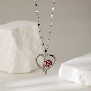 Zilveren hartketting met rode emaille roos en kristallen op een witte stenen achtergrond