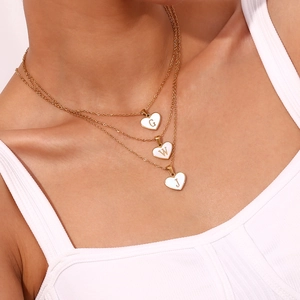 Detailopname van drie gelaagde 18K vergulde hartkettingen met letterhangers G W J
