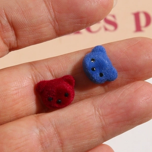 Macro shot of miniature flocked bear head charms in red and blue held by fingers