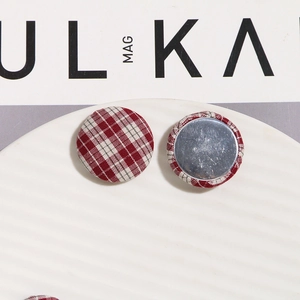 Macro detail of red and white plaid fabric covered buttons with a metal base on a tray