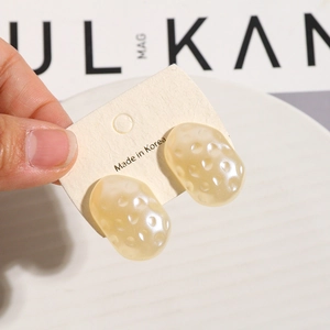 Detail of irregular white pearl acrylic earring studs with textured surface on a display card