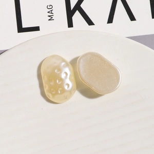 Detailed view of textured and smooth champagne resin pebble charms on a white ceramic tray